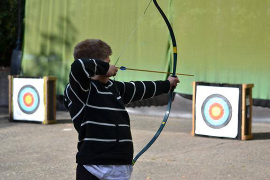 A boy aiming a bow and arrow at a target